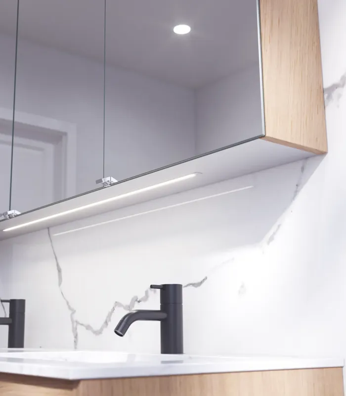 Bathroom inspiration with washbasin cabinets and wall cabinets in light oak with grooves, elegant double sink, beautiful mirror cabinet with light, herringbone floor in light wood, and white marble wall give a classic, bright, and sleek look.