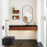 Modern and stylish bathroom inspiration with an oval mirror with a black frame and light control, colored toilet, vanity unit, base cabinets, and cabinets in reddish-brown oak, Silestone sink and matching floor