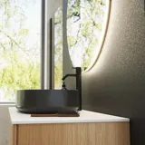 Minimalist and sleek bathroom inspiration with vanity unit, base cabinets, and tall cabinets in golden oak, large round mirror with light control, colored toilet, and countertop sink