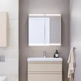 Small bathroom inspiration with a vanity unit and cabinet above the toilet in a beige custom color, elegant mirror cabinet with integrated lighting, the light colors and white curtain create a romantic and feminine atmosphere.
