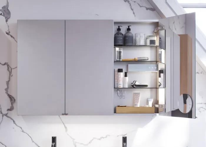 Bathroom inspiration with washbasin cabinets and wall cabinets in light oak with grooves, elegant double sink, beautiful mirror cabinet with light, herringbone floor in light wood, and white marble wall give a classic, bright, and sleek look.