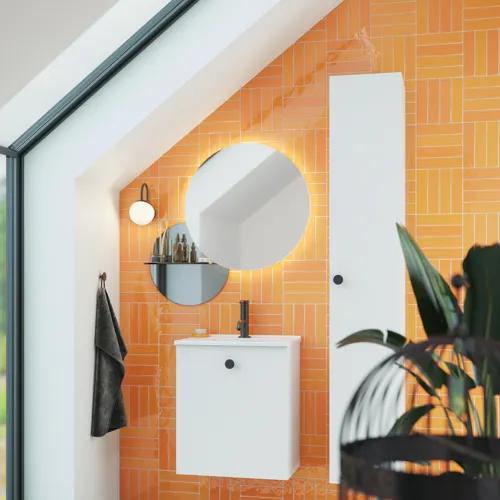 Bathroom with sloping ceiling inspiration with small white vanity unit and tall cabinet with round black handles, as well as beautiful round mirror, orange tiles give a fresh and modern look.