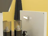 Small bathroom inspiration with a white vanity with black handle and black elegant sink, beautiful round mirror with black edge, offset wall cabinets, and terrazzo wall and floor, as well as yellow walls, provide a bold and modern look.