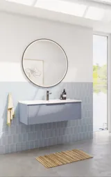 Bathroom inspiration with elongated light blue tiles and concrete floor, elegant light blue vanity unit with beautiful narrow stripes, sleek and thin sink, double tall cabinet with narrow stripes, and a minimalist round mirror with a black edge and light.