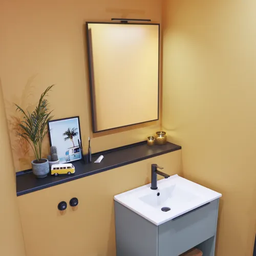Small bathroom inspiration with slanted and warm yellow walls, elegant light blue vanity unit, thin and sleek sink, and minimalist square mirror with a black edge and practical lamp.
